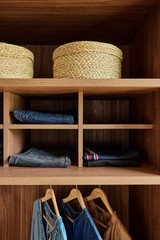 Étagères en bois foncé avec paniers de rangement en osier et jeans soigneusement pliés dans un dressing ouvert.