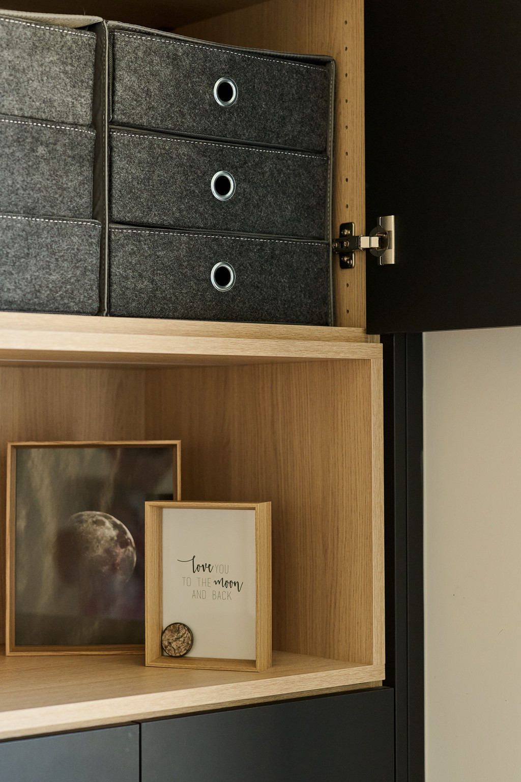Niche ouverte en bois avec cadres décoratifs et rangements en tissu dans une armoire sur mesure aux portes noires