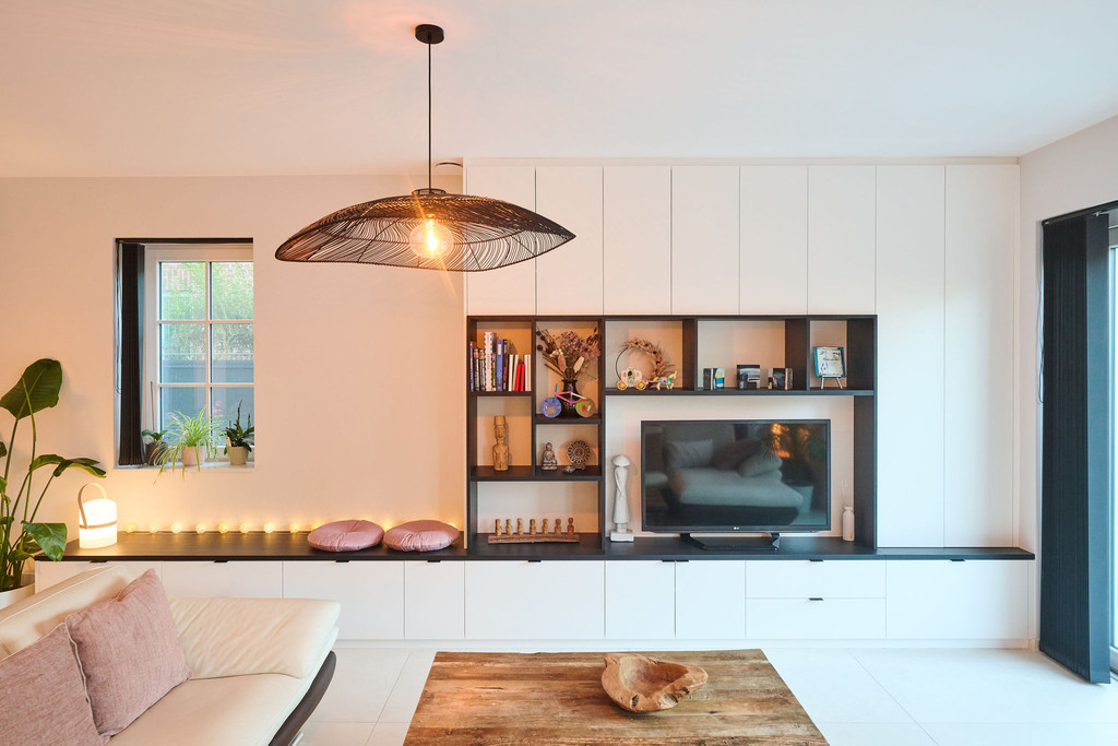 Witte wandkast op maat met open vakken en tv meubel, ingericht met decoratieve objecten en verlichting in de woonkamer.