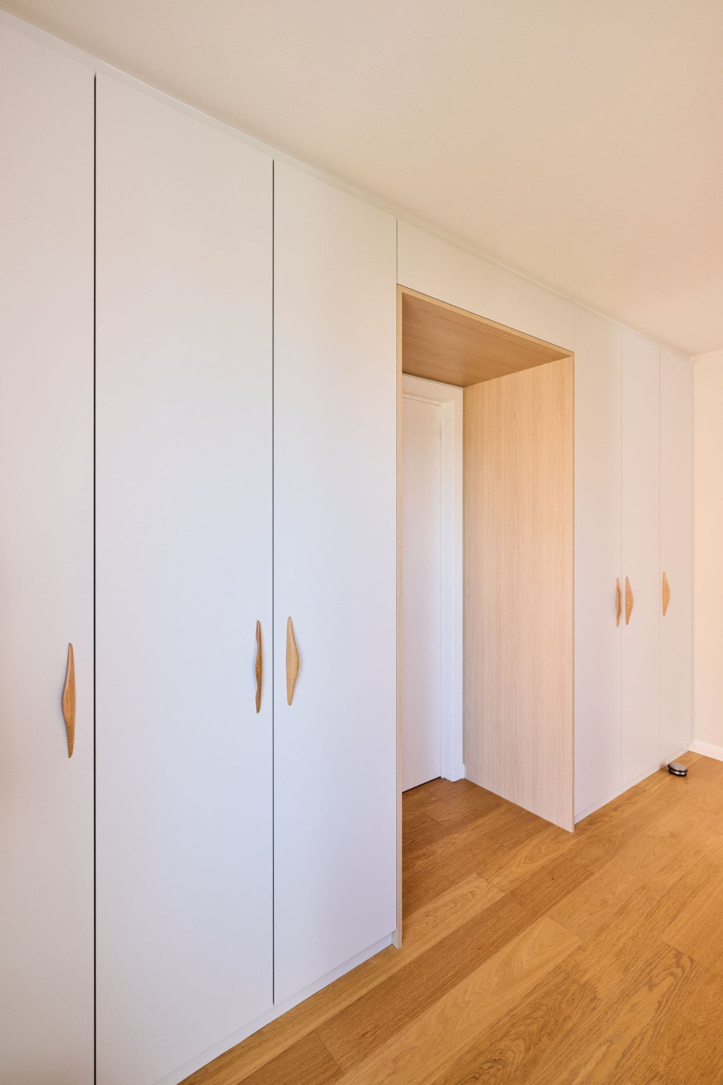 Dressing sur mesure avec portes blanches et passage en bois vers une pièce adjacente dans une chambre