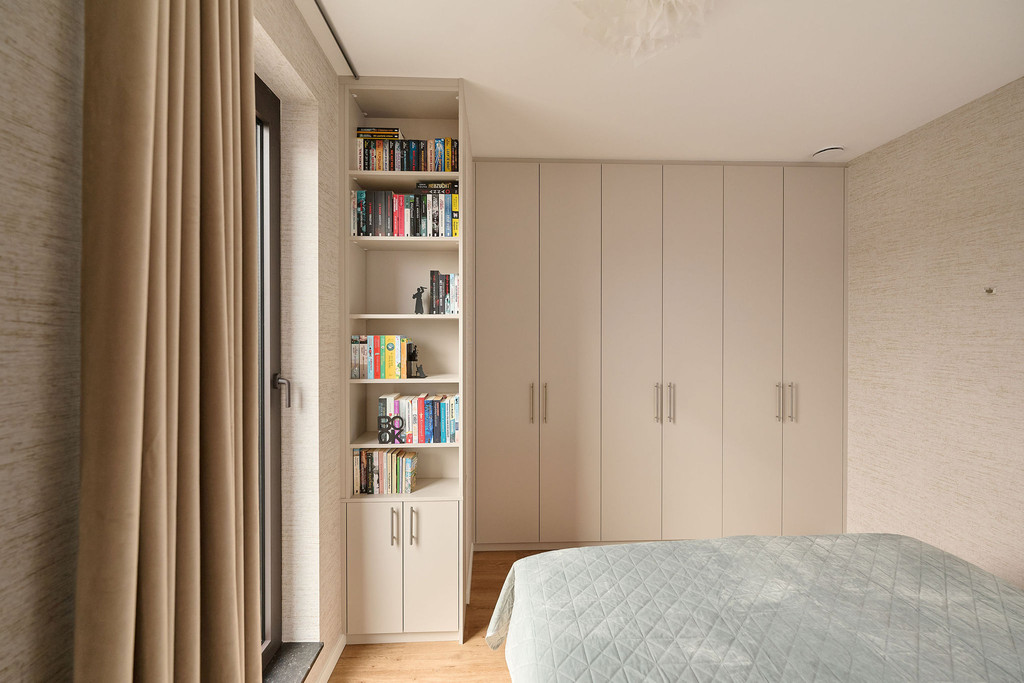 Dressing sur mesure avec portes en tons clairs et bibliothèque ouverte intégrée près de la fenêtre, combinant rangement et espace pour livres dans une chambre lumineuse, réalisé par Camber