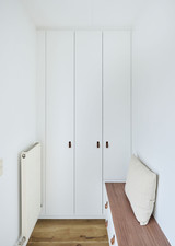 Meuble de vestiaire sur mesure blanc avec des portes lisses et un banc intégré en bois clair, idéal pour une entrée ou un hall.