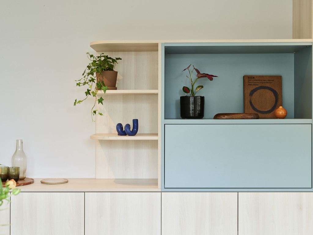 Op maat gemaakte kast met blauwe schuifdeur en open planken voor decoratie in woonkamer.