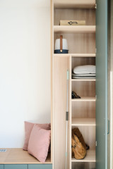 Placard ouvert avec étagères en bois clair et coussin rose sur banquette verte