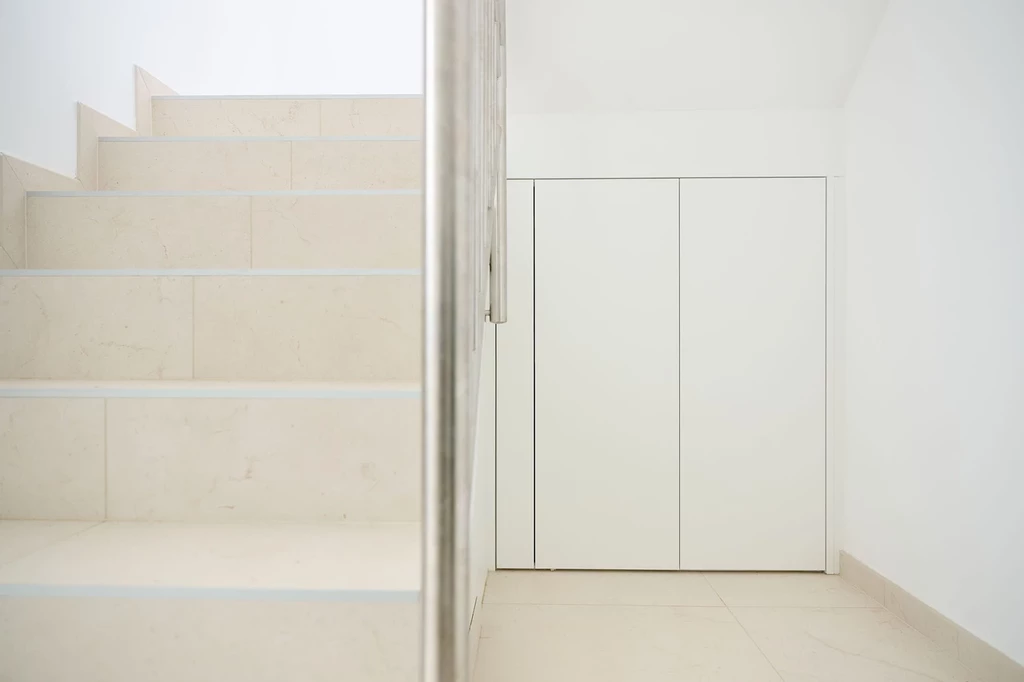 Witte ingemaakte kast onder een trap met strakke afwerking en greeploze deuren, optimaal gebruik van de ruimte onder de trap.