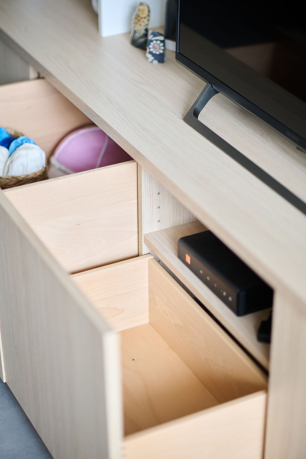 Tiroir ouvert d’un meuble TV avec intérieur en bois et espace de rangement pour pelotes et électronique