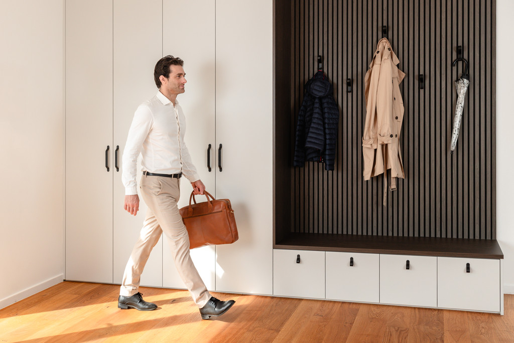 Man met aktetas loopt door inkomhal langs een op maat gemaakte vestiairekast met kapstokhoek.