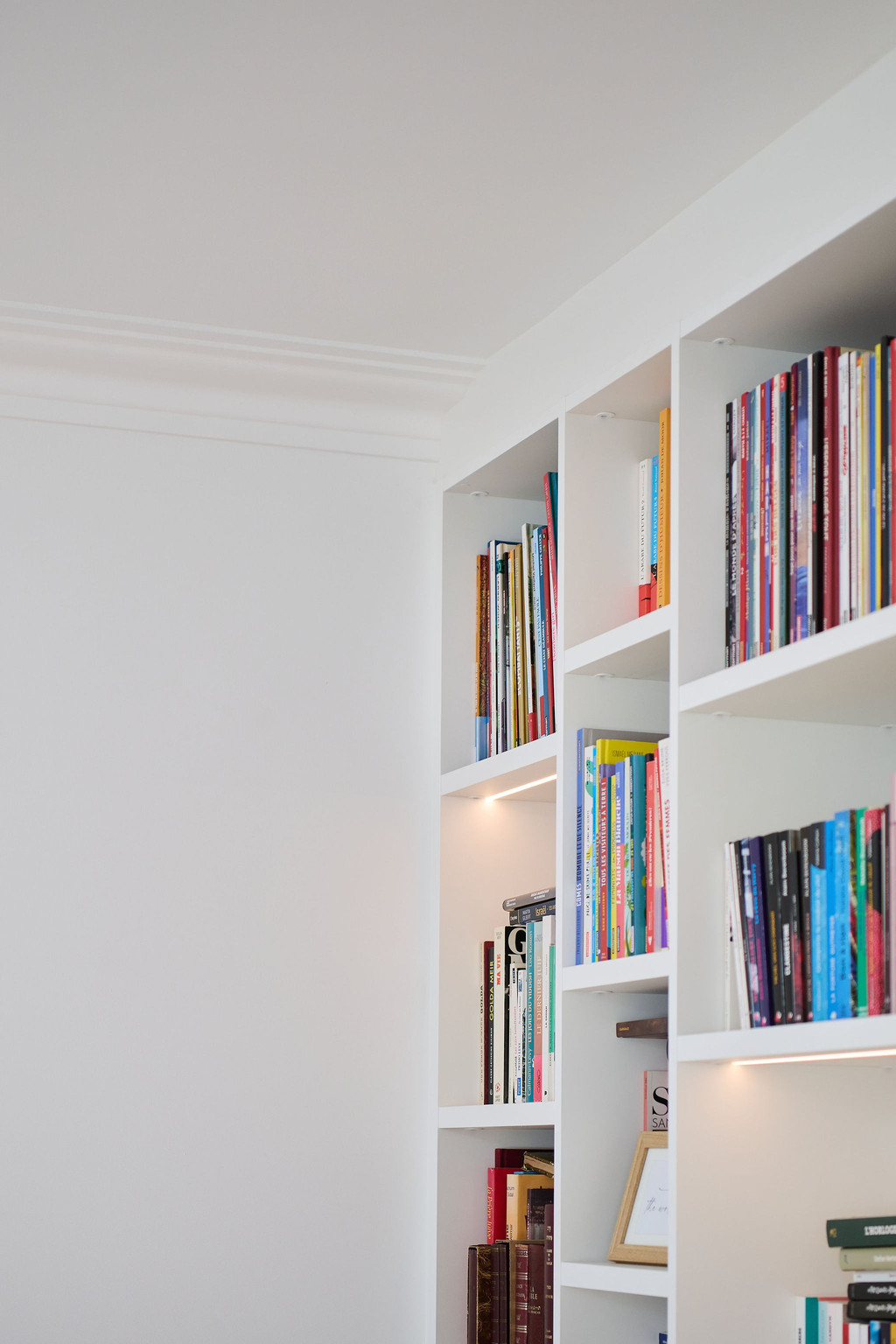 Witte boekenkast op maat met led verlichting afgewerkt rond plafondlijst