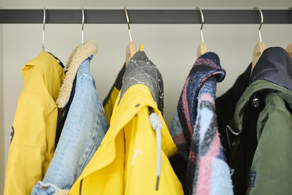 Verschillende jassen aan houten kleerhangers op een zwarte roede in een vestiairekast