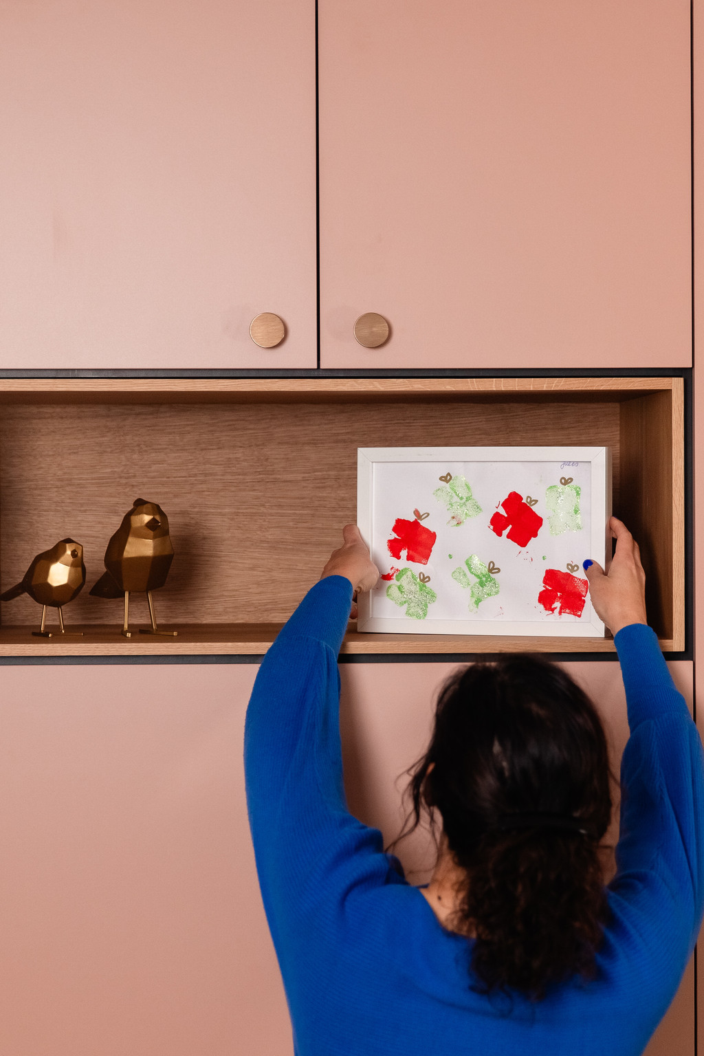 Een vrouw plaatst een tekening in de open nis van een roze maatkast met houten afwerking. De decoratieve details en warme tinten zorgen voor een persoonlijke en harmonieuze inrichting.
