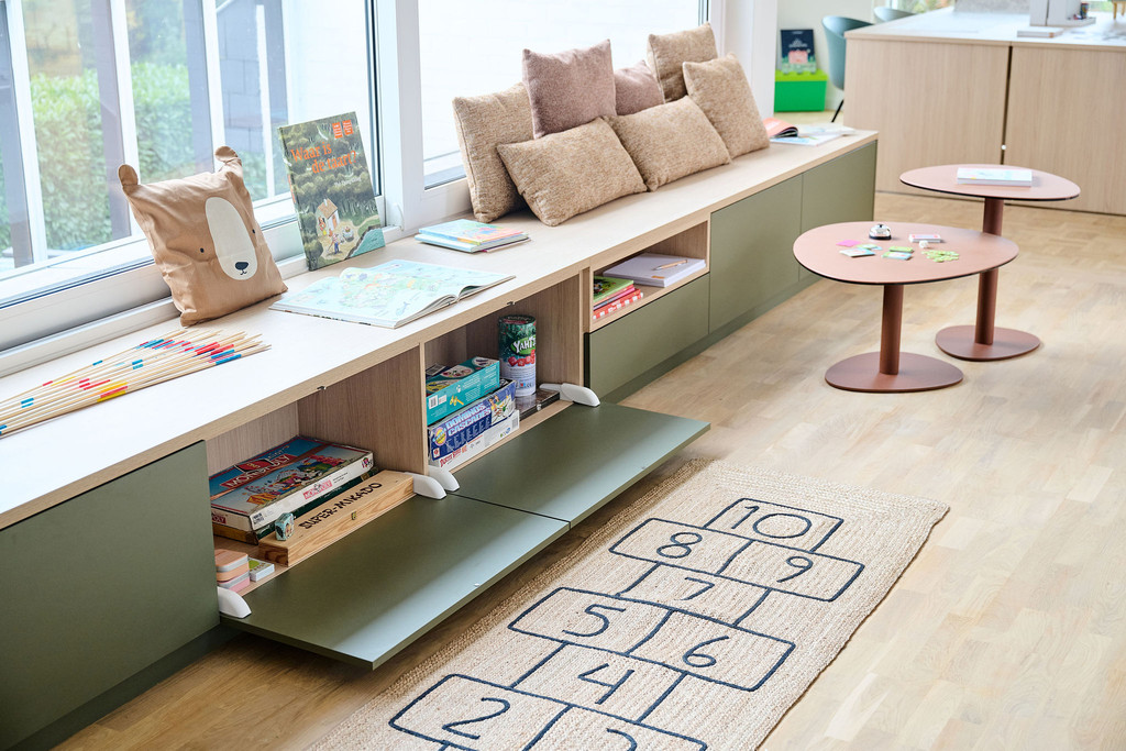 Op maat gemaakte zitbank met beige kussens en open klepkasten gevuld met boeken en spelletjes