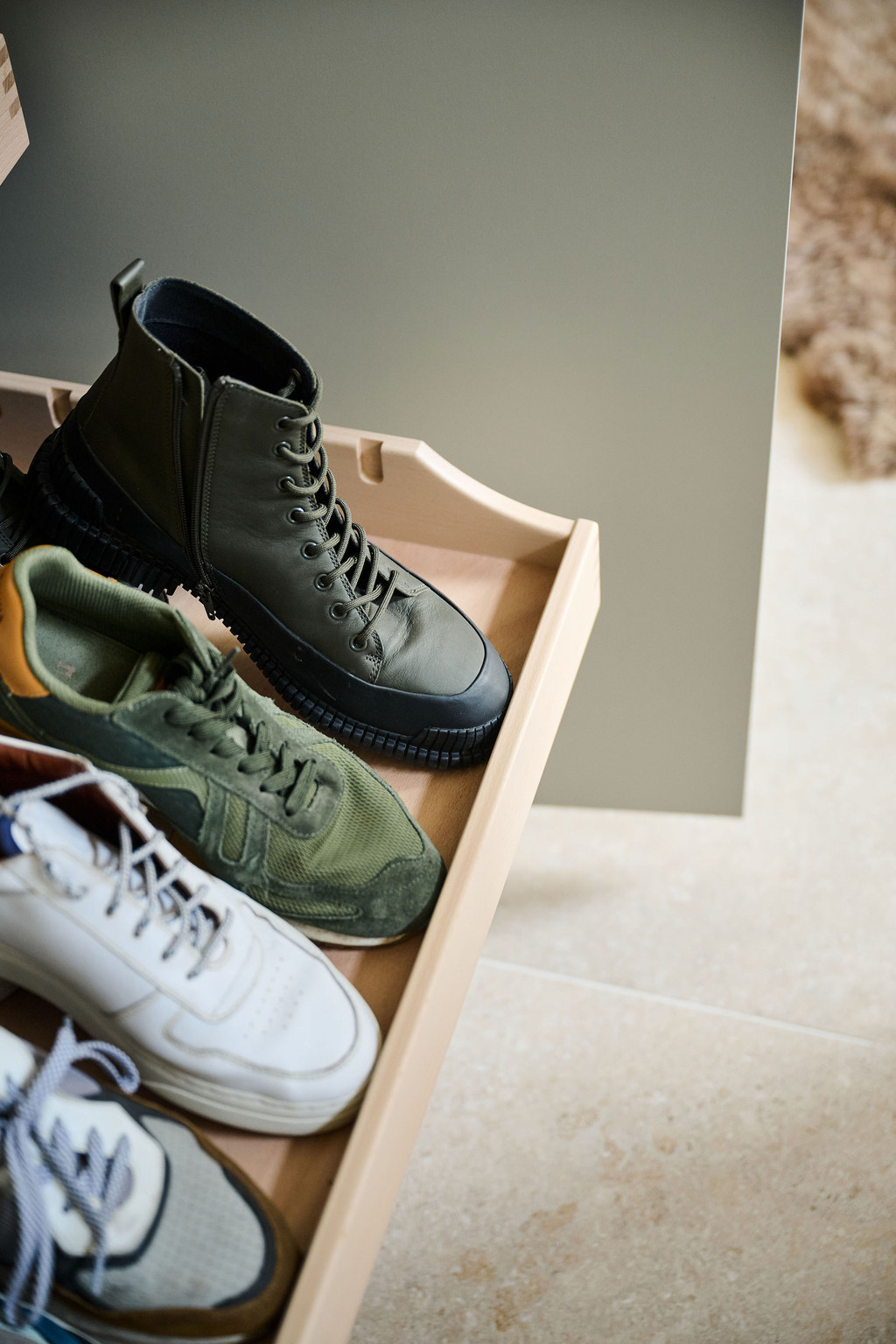 Gros plan sur un tiroir coulissant en bois avec plusieurs paires de chaussures dans une armoire d’entrée blanche