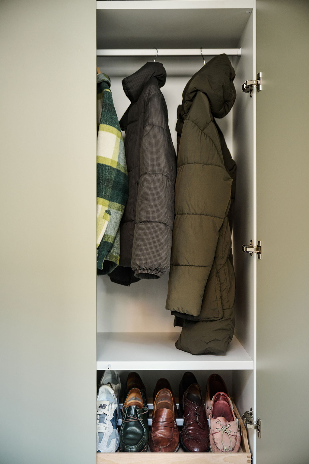 Partie ouverte d’une armoire avec manteaux suspendus et étagère inférieure visible dans une vestiaire blanche
