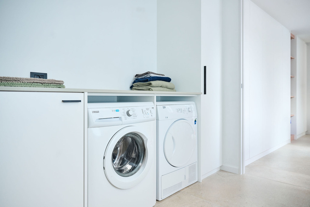 Buanderie blanche avec machine à laver et sèche-linge encastrés sous un plan de travail dans une maison moderne