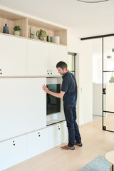Homme ouvrant la porte coulissante d’un meuble sur mesure blanc avec niche TV dans un salon moderne