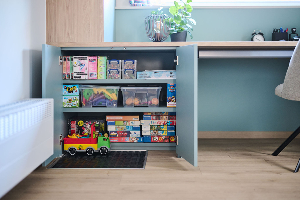 Armoire basse ouverte avec jeux et jouets dans un bureau bleu sur mesure avec plan de travail en bois
