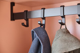 Detail van een Camber vestiaire op maat met metalen jashaken op rail, geïntegreerd in een open nis met zachte kleurafwerking