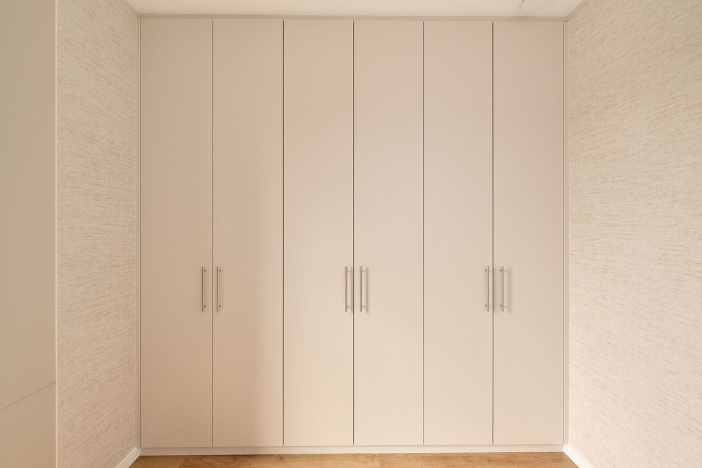 Grand dressing sur mesure avec portes en tons clairs et poignées élégantes, offrant une solution de rangement discrète et harmonieuse dans une chambre, réalisé par Camber