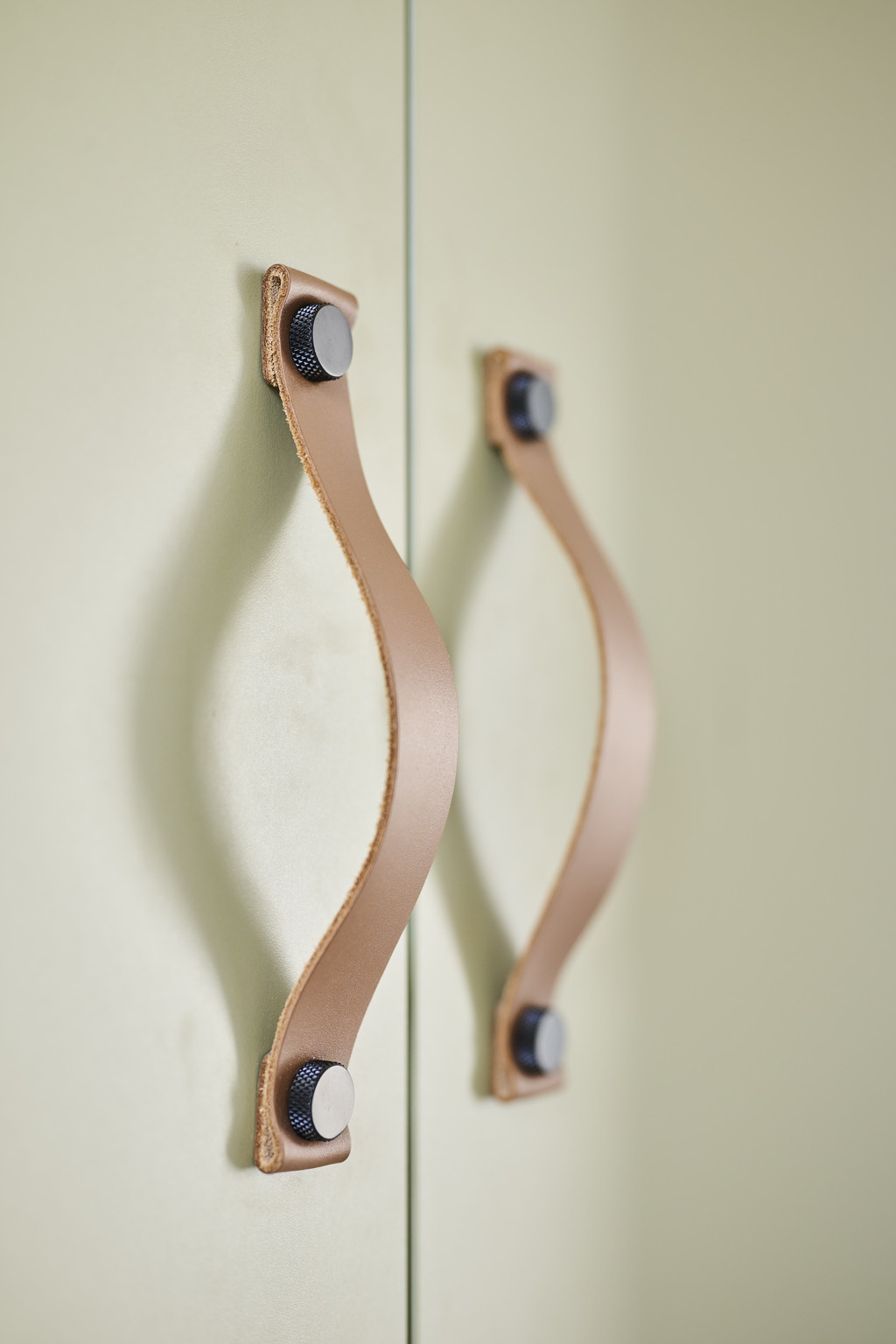 Détail d’une porte de placard verte avec poignées en cuir et fixations noires