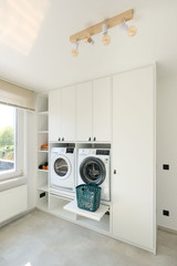 Femme devant un meuble de buanderie blanc avec machines intégrées et panier à linge