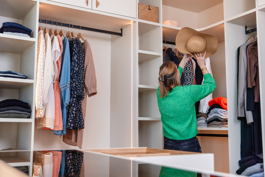 Femme range un chapeau d'été dans un dressing blanc sur mesure avec niches ouvertes et tiroir vitré
