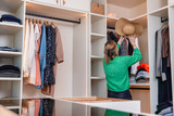 Femme range un chapeau d'été dans un dressing blanc sur mesure avec niches ouvertes et tiroir vitré