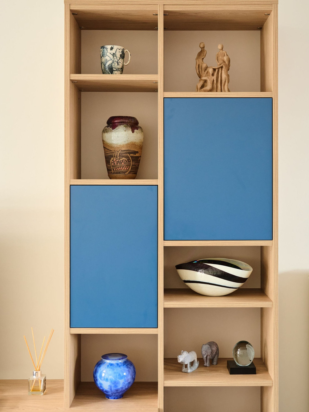 Detail van een houten wandkast op maat met open nissen voor decoratie en gesloten opbergvakken met blauwe fronten