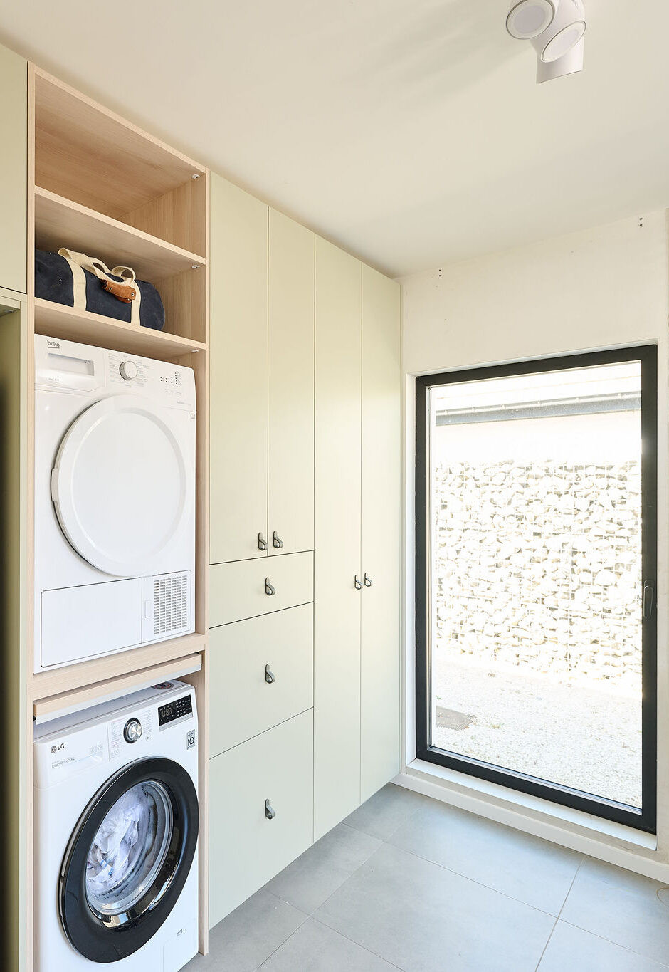 Vue d’ensemble d’une buanderie Camber sur mesure avec machine à laver et sèche-linge en colonne, réfrigérateur intégré, placards fermés et niches ouvertes dans un aménagement fonctionnel