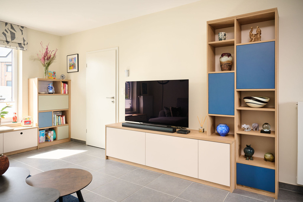 Tv-meubel op maat met witte gesloten kasten, houten bovenblad en hoge wandkast met open vakken en blauwe accenten