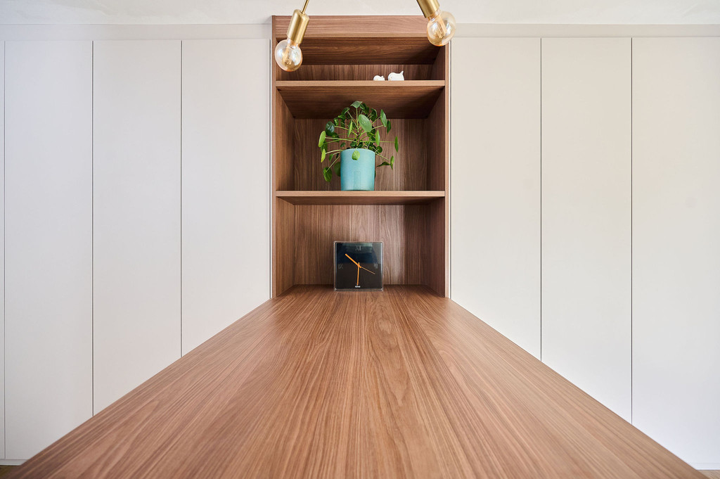 Détail d’une niche ouverte en décor bois avec étagères, intégrée dans une armoire sur mesure blanche avec plan de travail en bois