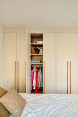 Armoire sur mesure ouverte avec vêtements suspendus et étagères organisées dans une chambre