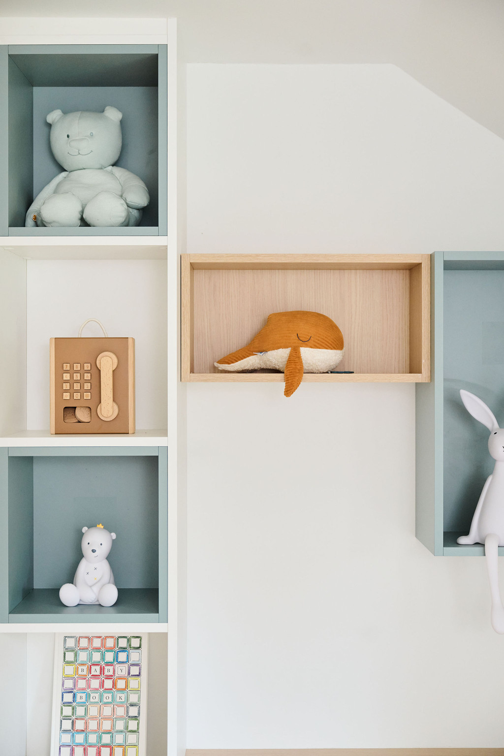 Détail d'étagères avec des figurines et jouets pour enfants, incluant une figurine en bois et un chapeau orange.