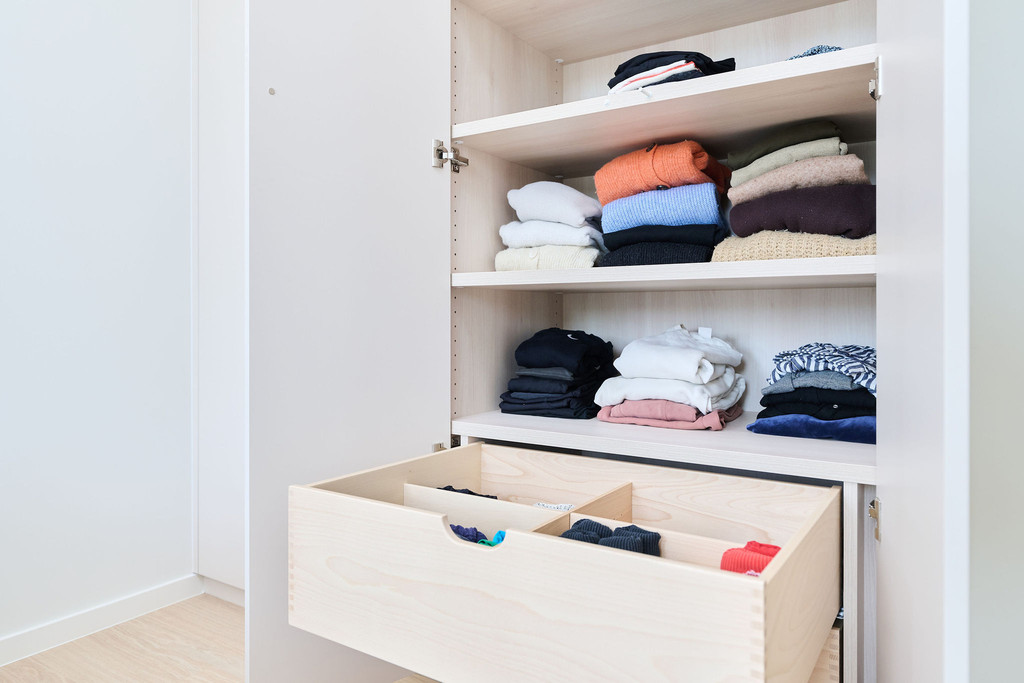 Tiroir ouvert avec compartiments sous des étagères dans une armoire sur mesure avec vêtements pliés