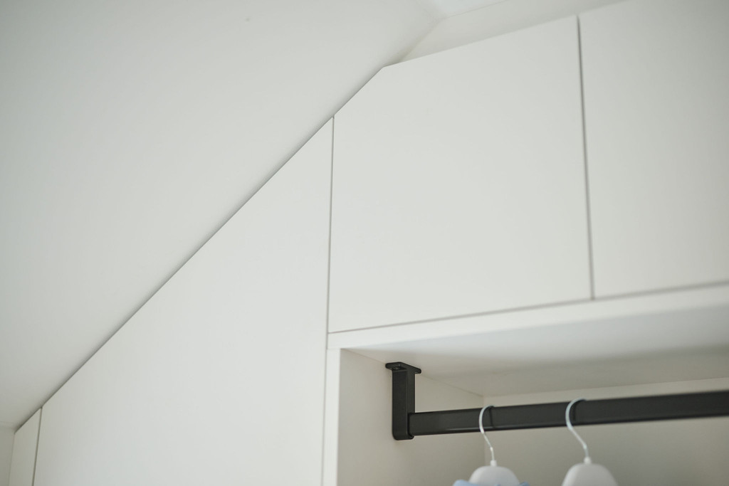 Rangement buanderie sur mesure avec tringle de penderie sous pente, finitions soignées et design optimisé pour les espaces sous les toits.