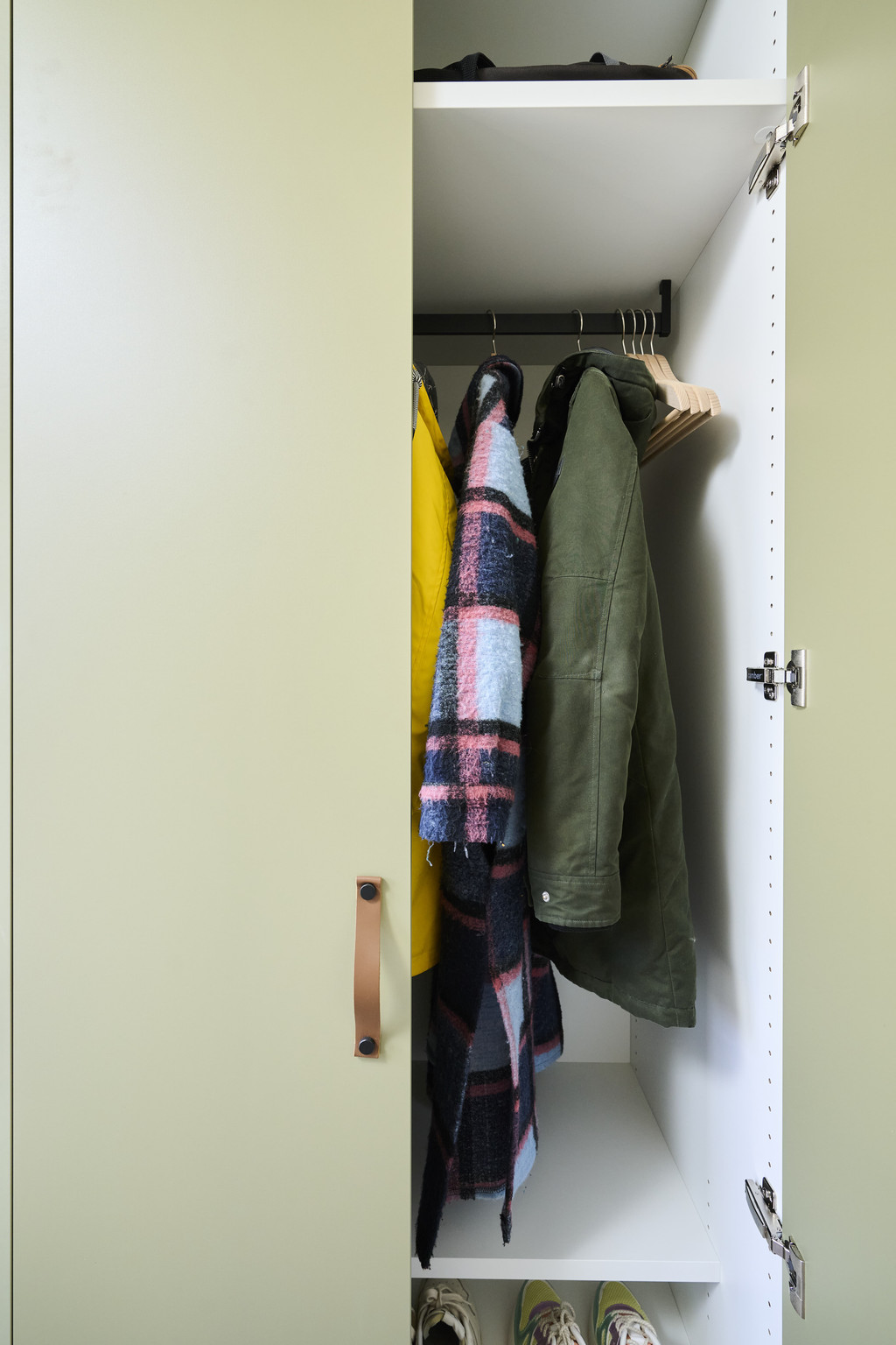 Halfopen maatkast in groene kleur met jassen aan wandkapstok in inkomhal