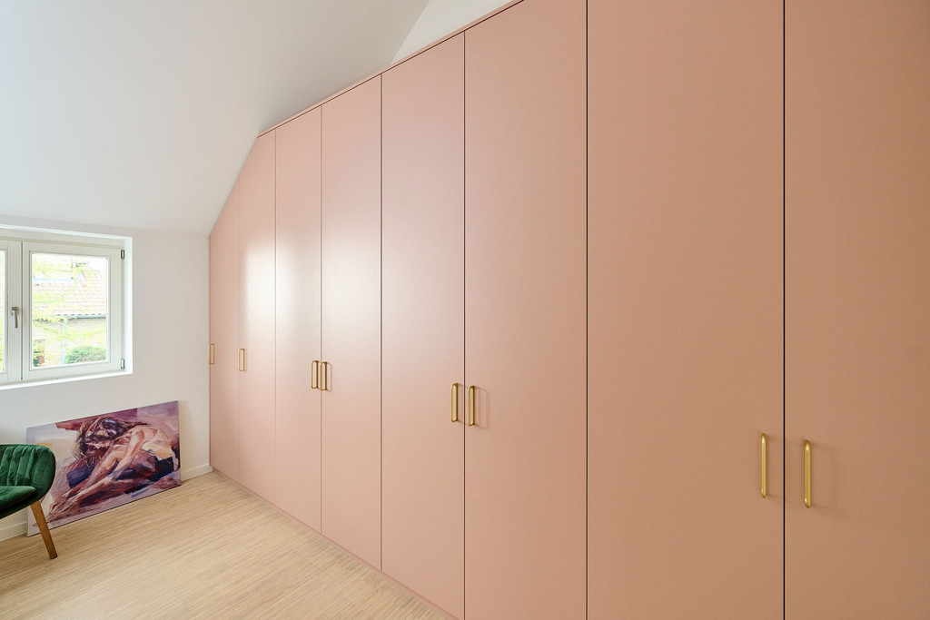 Op maat gemaakte gesloten dressing met roze deuren en gouden handgrepen onder een schuin dak.