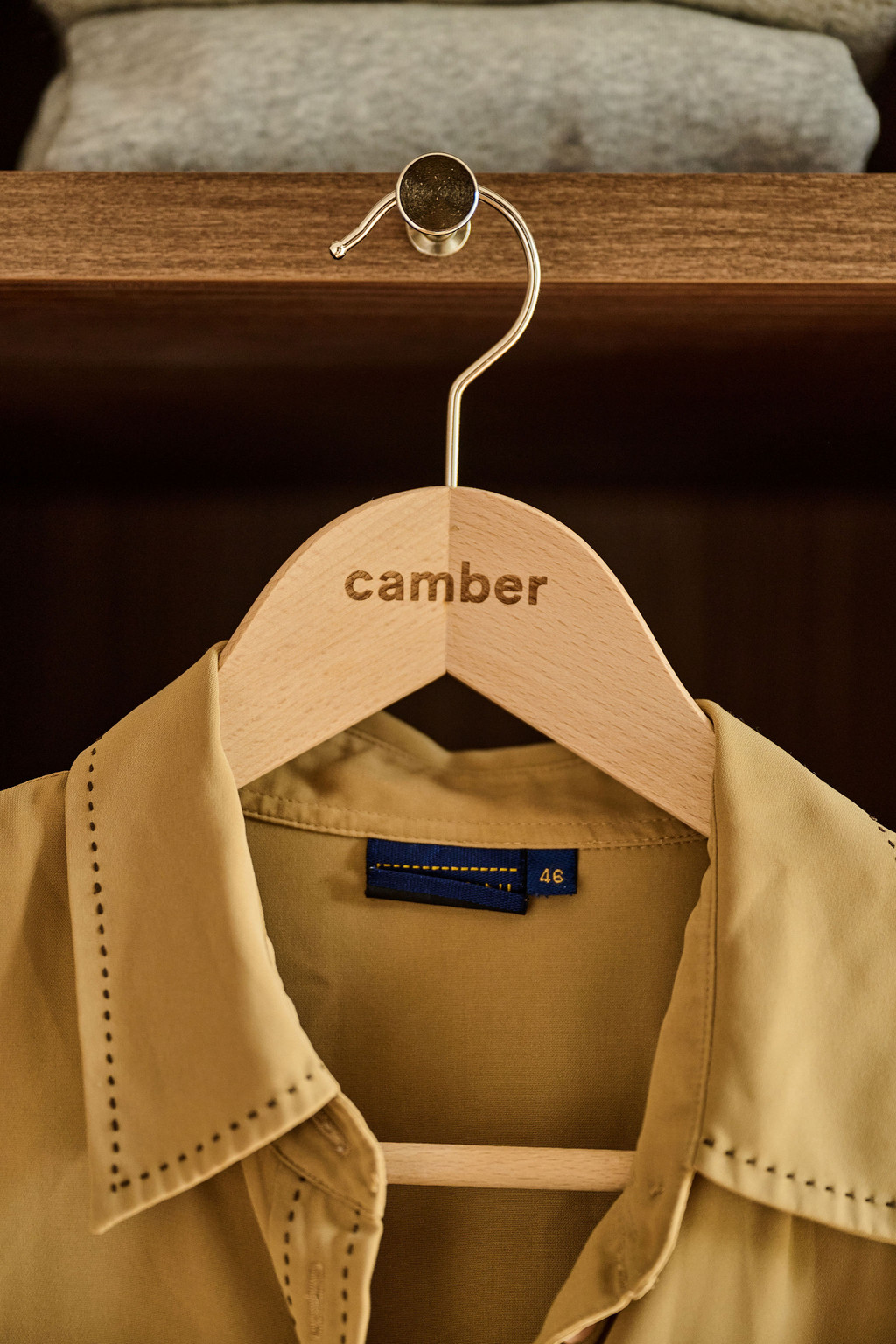 Cintre en bois avec chemise beige suspendue dans un dressing ouvert en bois foncé, offrant un rangement élégant et fonctionnel.