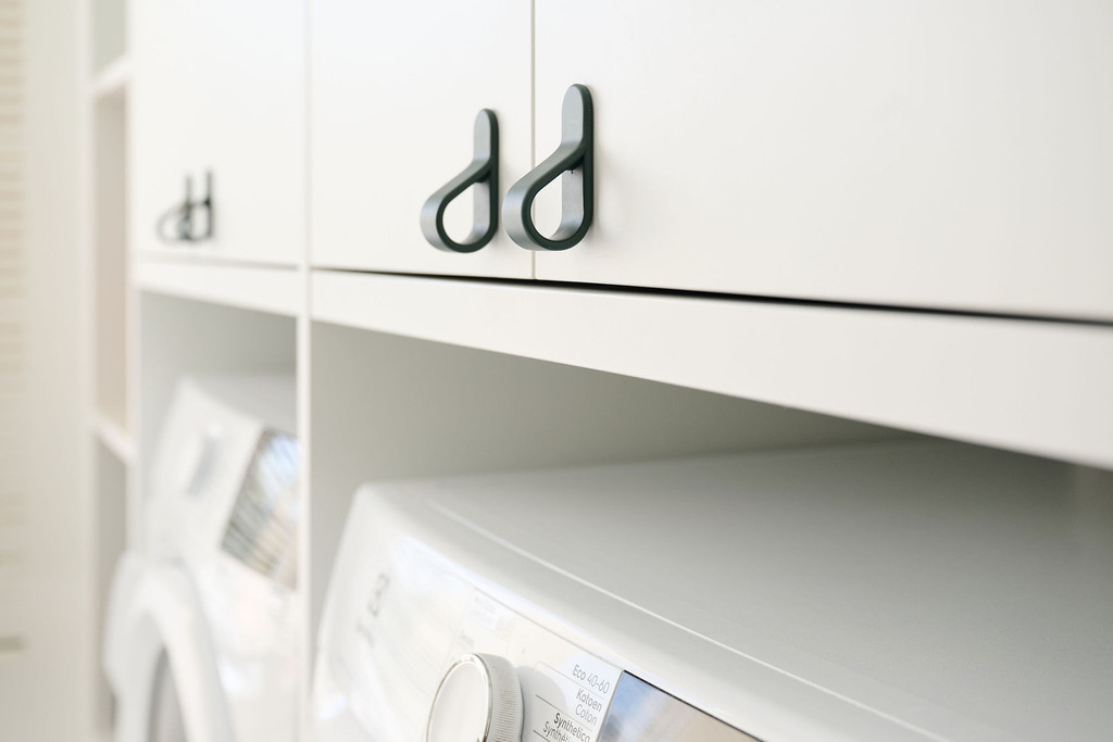 Poignées vert foncé sur meuble sur mesure blanc au-dessus d’un lave-linge intégré