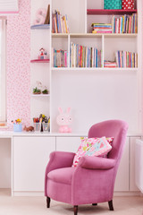 Meuble de rangement sur mesure avec étagères et espace de travail pour chambre d’enfant avec fauteuil rose.