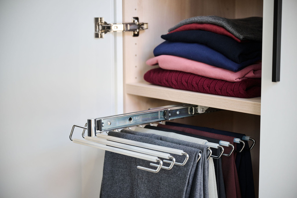 Uittrekbare broekhouder in houten maatkast onder legplank met opgevouwen truien in een praktische dressing