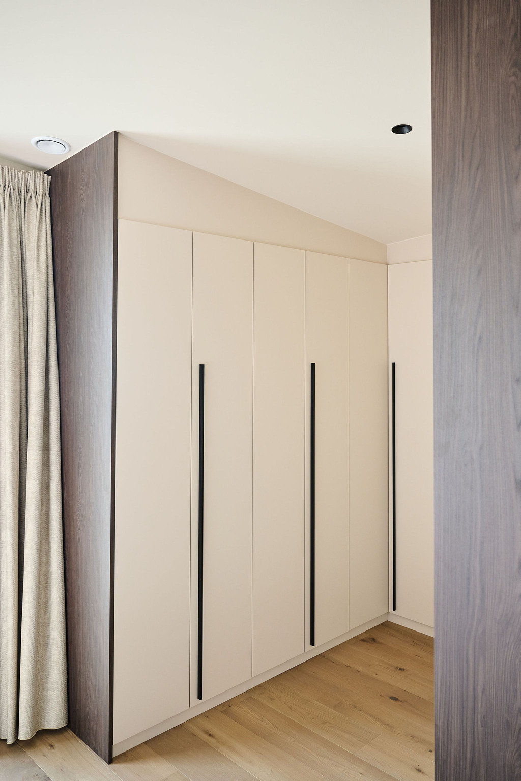 Grand dressing sur mesure avec portes en tons clairs et longues poignées métalliques noires, intégré sous pente pour une optimisation maximale de l’espace, réalisé par Camber