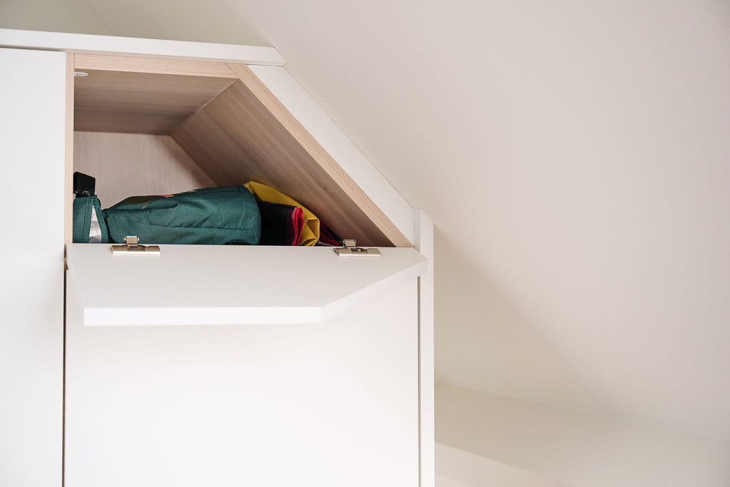 Placard sur mesure sous pente avec rangement dissimulé derrière un panneau dans une chambre d’enfant