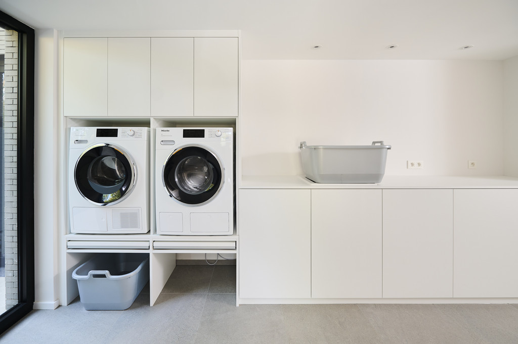 Espace buanderie moderne sur mesure avec lave-linge et sèche-linge encastrés et meuble de rangement pratique.