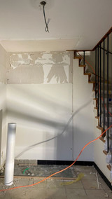 Inkomhal in renovatie met deels afgebikte muur onder houten trap en oude vloerbekleding