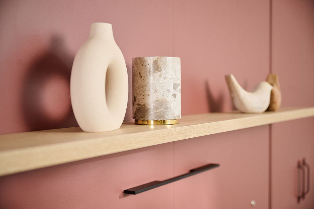 Étagère décorative en bois avec des objets d'art et des vases modernes, mise en valeur sur un fond rose doux.