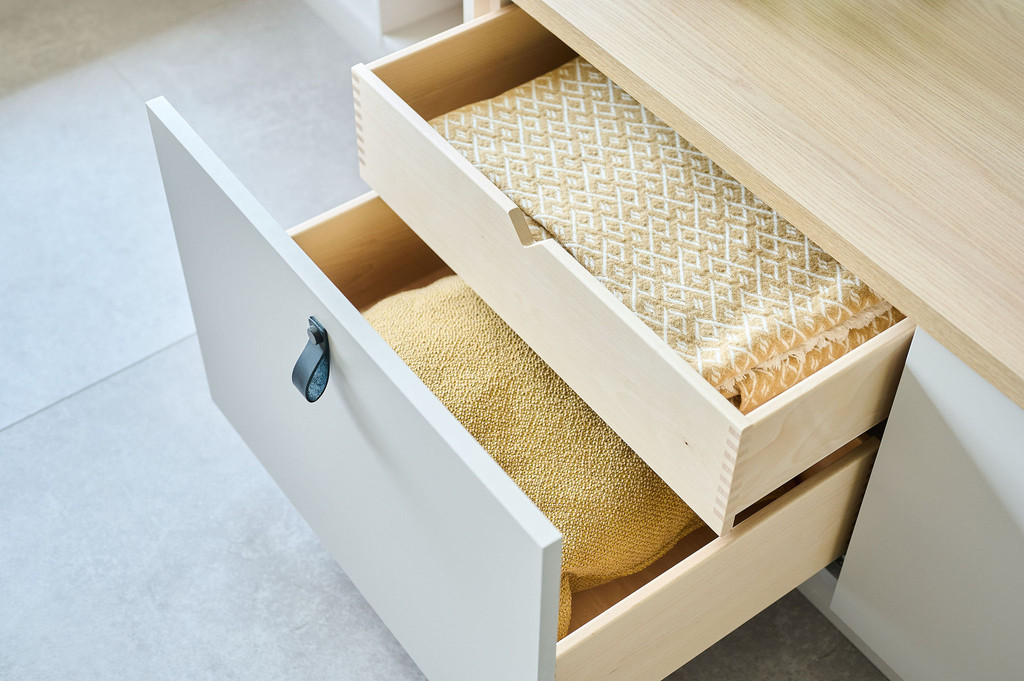 Détail de tiroirs sur un meuble bas de salon sur mesure, avec coussins pliés et finition soignée.