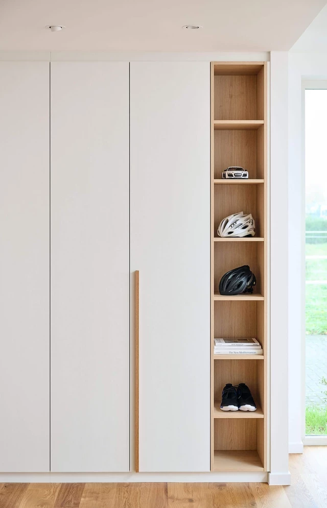 Ingebouwde witte dressingkast op maat met open houten vakken voor sportaccessoires, boeken en schoenen.