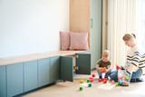Banquette sur mesure verte avec coussins et armoires basses ouvertes dans une pièce lumineuse avec jouets