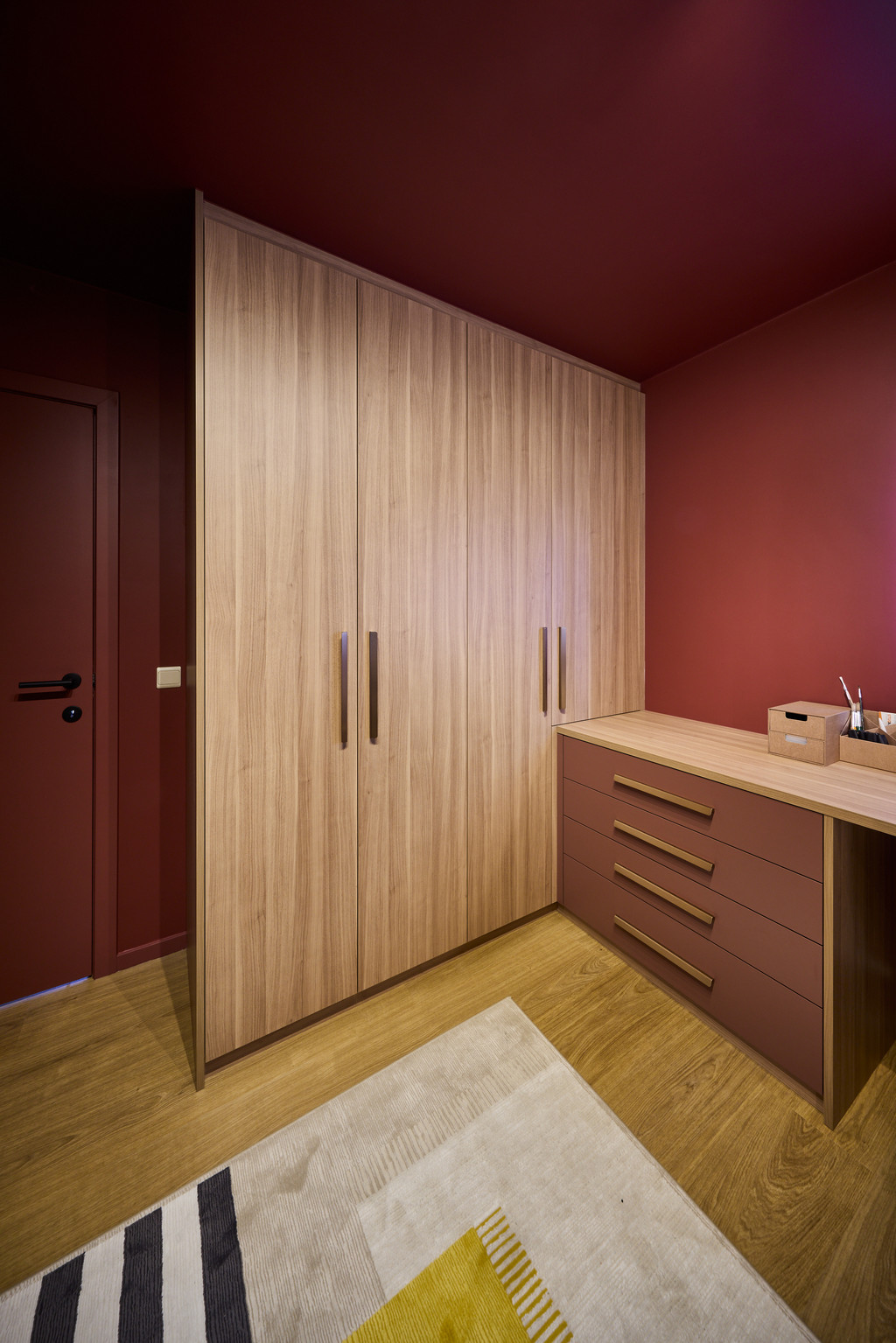 Maatkast onder schuine wand met houten deuren en geïntegreerd bureau in een warme slaapkamer