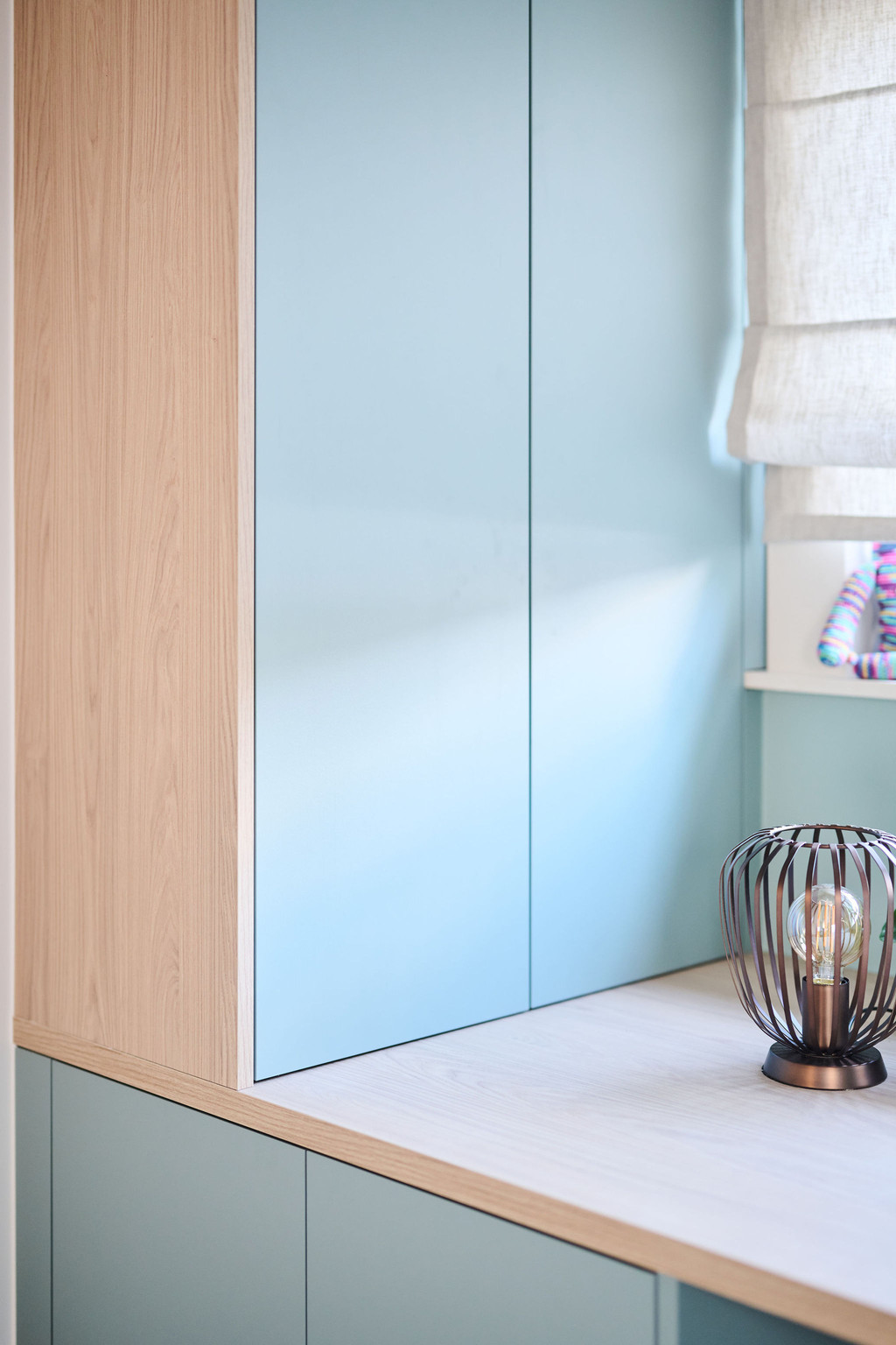 Détail d’un module d’armoire bleu fermé avec côté en bois et vase décoratif dans un bureau lumineux